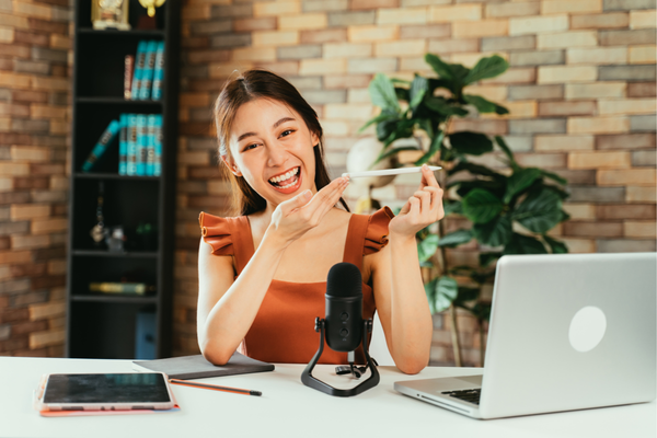 Một nữ influencer trẻ trung đang cười tươi khi quay video quảng bá sản phẩm trước micro, với laptop và tablet đặt trên bàn – biểu tượng cho xu hướng influencer marketing hiện đại.